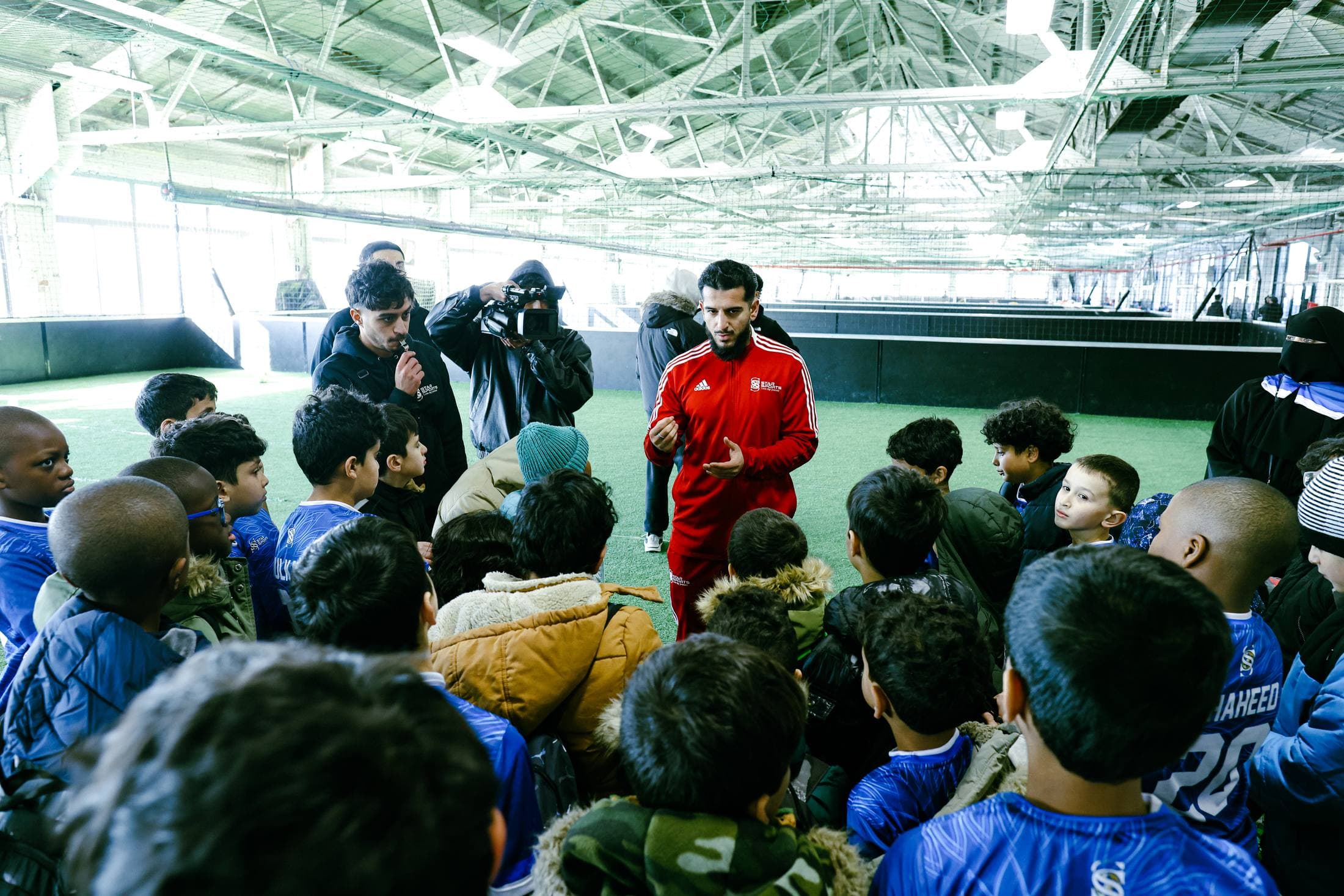 Founder Sanawullah Shairzai talks with a group of young players on an indoor field